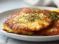 Goldbraune Kartoffelpuffer im Airfryer, garniert mit frischer Petersilie, auf einem weißen Teller.