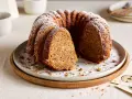Ein saftiger Kuchen mit Dinkelmehl, bestäubt mit Puderzucker, liegt auf einem Teller. Ein Stück ist herausgeschnitten.