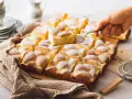 Ein Stück Spiegeleikuchen mit Quark wird aus einem Blechkuchen mit Puderzucker gehoben.