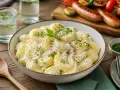 Cremiger Kartoffelsalat mit Schmand, garniert mit frischer Petersilie, bereit für ein Grillfest.