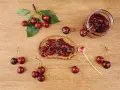 Frisches Brot mit Kirschmarmelade, garniert mit Minze. Ein Glas Kirschmarmelade und frische Kirschen daneben. Perfekt für ein Kirschmarmelade Rezept.
