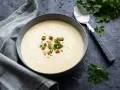 Cremige Spargelsuppe aus Schalen, garniert mit Croutons und frischen Kräutern. Ein Löffel liegt daneben.