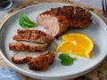 Saftige entenbrust im airfryer, perfekt gebräunt und in Scheiben geschnitten, serviert mit frischen Orangenscheiben und grünen Blättern.