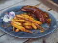 Eine saftige Currywurst im Backofen mit knusprigen Pommes und einem Klecks Mayo mit Zwiebeln.