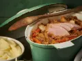 Herzhafter Szegediner Gulasch mit zarten Fleischscheiben, Sauerkraut und Karotten in einem grünen Topf, daneben eine Schüssel cremiges Kartoffelpüree.