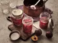 Frisch eingekochte Pflaumenmarmelade im Glas, bereit für das pflaumenmarmelade rezept. Frische Pflaumen liegen daneben.