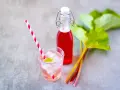 Erfrischendes Getränk mit Rhabarbersirup, Eis und Minze. Frische Rhabarberstangen und Blätter deuten auf ein leckeres Rhabarbersirup Rezept hin.