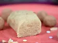 Ein Block selbstgemachtes Marzipan, ohne Rosenwasser, liegt auf einer roten Platte. Daneben sind Pralinen und bunte Zuckerstreusel.