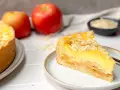 Ein saftiger Apfelkuchen mit Schmandguss, bestreut mit Mandelblättchen. Daneben liegen frische Äpfel.