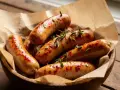 Saftige bratwurst im airfryer, goldbraun und mit Rosmarin garniert, serviert in einer Holzschale auf rustikalem Tisch.