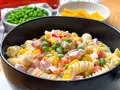 Ein cremiger nudelsalat mit mayonaise, garniert mit Erbsen, Mais, Paprika und Schinkenwürfeln.