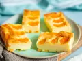 Vier Stücke saftiger Mandarinen Quark Kuchen auf einem Teller, garniert mit frischen Mandarinenstücken.