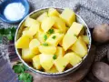 Schüssel mit dampfenden Salzkartoffeln, garniert mit Petersilie. Daneben eine kleine Schale mit Salz und rohe Kartoffeln.