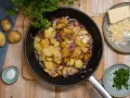 Bratkartoffeln mit Zwiebeln und Käse in der Pfanne, dazu frische Petersilie und Salz.