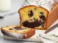 Ein saftiger marmorkuchen mit Puderzucker bestäubt, daneben ein Stück Kuchen und ein Sieb. Perfekt mit einem Klecks Sahne.