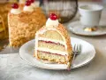 Ein Stück Frankfurter Kranz, das Rezept eines Konditors, mit Buttercreme und Kirschen verziert, umgeben von gehackten Nüssen.
