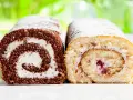 Zwei Biskuitrollen, eine schokoladig, die andere hell, mit Sahne und Fruchtfüllung, bestäubt mit Puderzucker. Wie von Landfrauen gebacken.