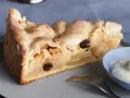 Ein Stück gedeckter Apfelkuchen mit Rosinen und Zuckerguss, serviert mit einem Klecks Sahne.