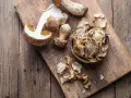 Frische und getrocknete Steinpilze liegen auf einem Holzbrett. Die getrockneten Pilze sind in einer Schale und daneben verteilt, bereit zum Kochen.