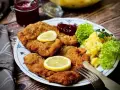 Knuspriges Wiener Schnitzel mit Zitrone, Preiselbeeren und Kartoffelsalat auf einem Teller.