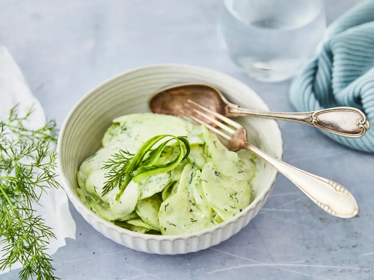 Omas Gurkensalat mit Joghurt, cremig und frisch, garniert mit Dill. Ein Löffel und eine Gabel liegen bereit.