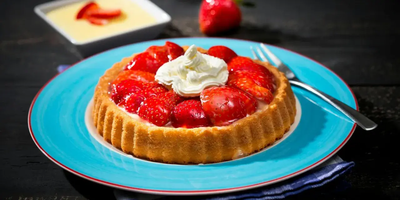 Erdbeerkuchen mit fertigboden, belegt mit frischen Erdbeeren und Sahne, auf einem blauen Teller.