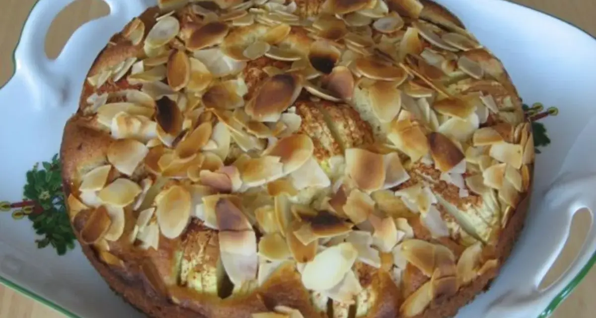 Ein köstlicher, kleiner Apfelkuchen mit gerösteten Mandelblättchen auf einer verzierten Servierplatte.