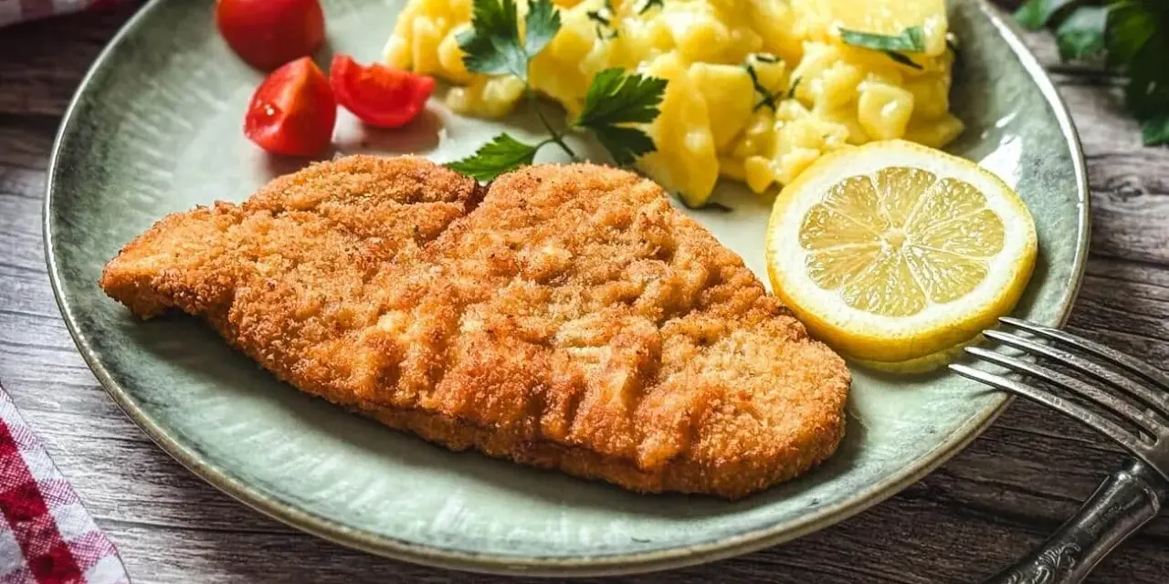 Perfekt gebratenes Putenschnitzel mit Kartoffelsalat, Tomaten und Zitrone auf einem Teller.