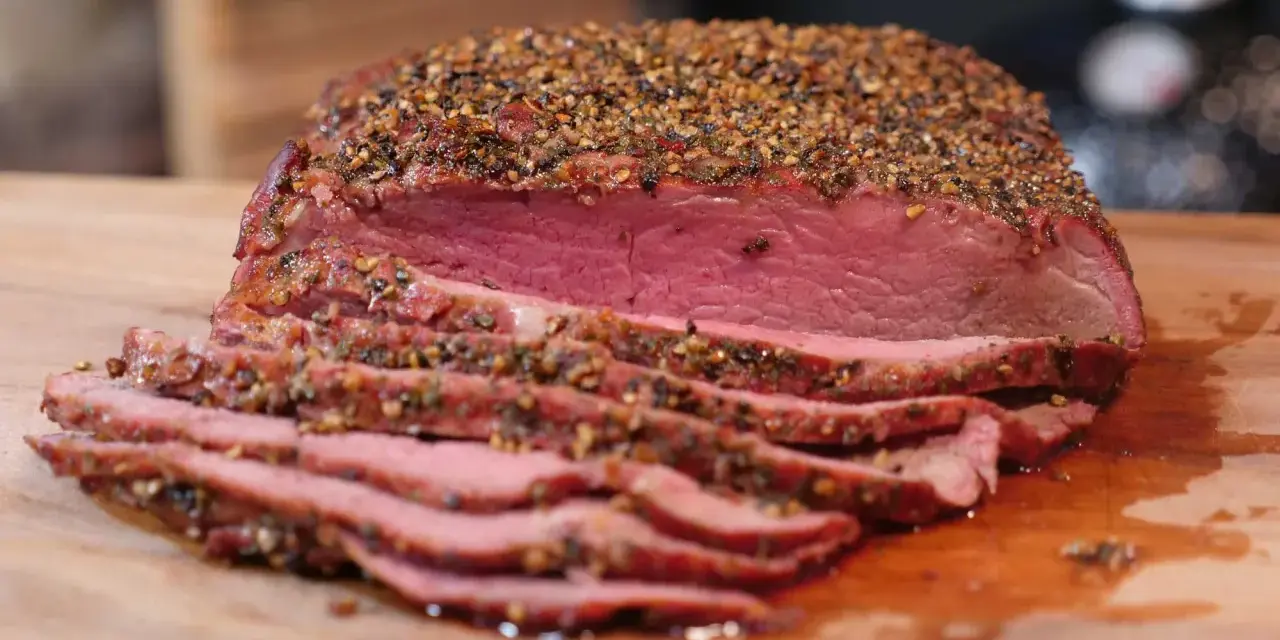 Perfekt gegarter Roastbeef Braten, saftig und rosa, mit einer würzigen Kruste aus Pfeffer und Kräutern, auf einem Holzbrett.