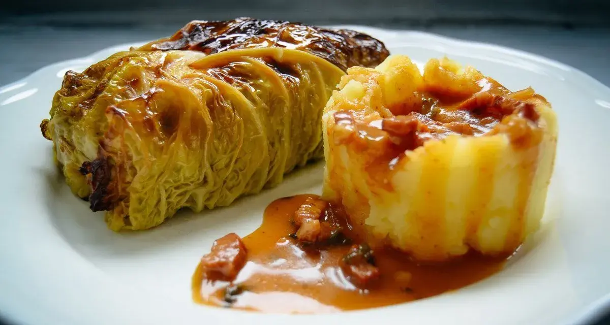 Ein goldbraunes Kohlrouladen-Rezept auf einem Teller, serviert mit Kartoffelpüree und einer herzhaften Sauce.