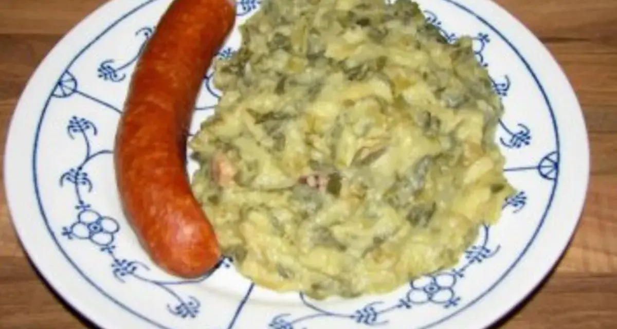 Omas Stielmus Rezept: deftiger Grünkohl mit Kartoffeln und einer herzhaften Bratwurst auf einem blau-weißen Teller.