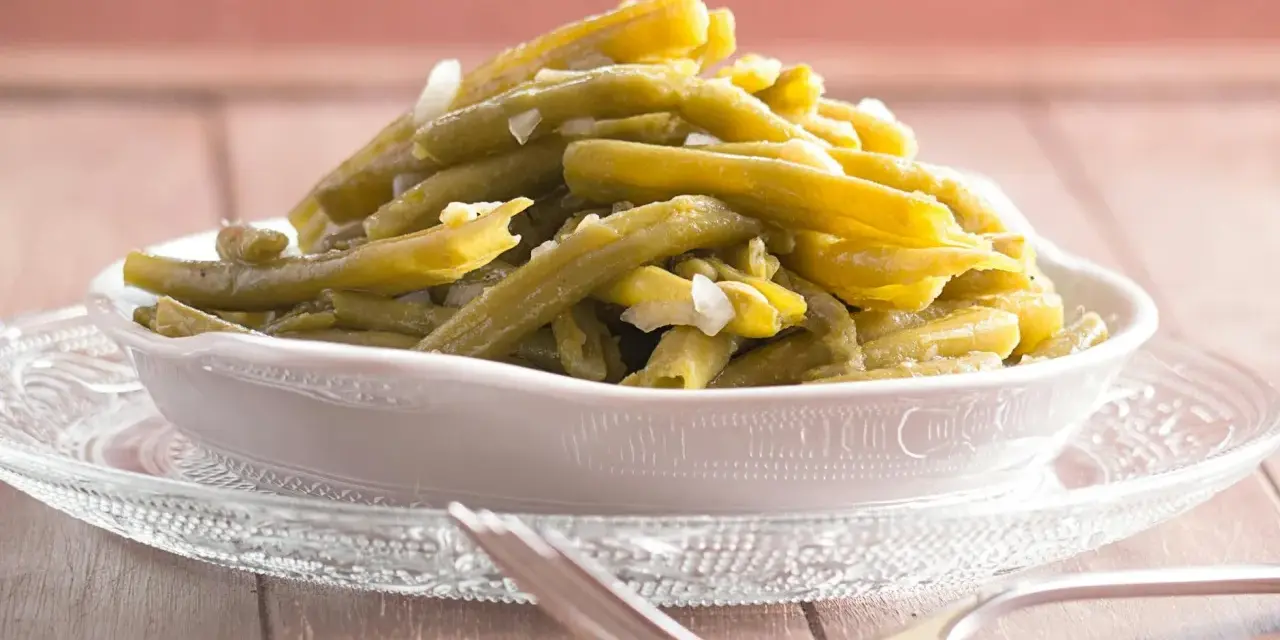 Omas Bohnensalat Rezept: Grüne Bohnen mit Zwiebeln in einer Schüssel auf einem Glasuntersetzer, daneben eine Gabel.