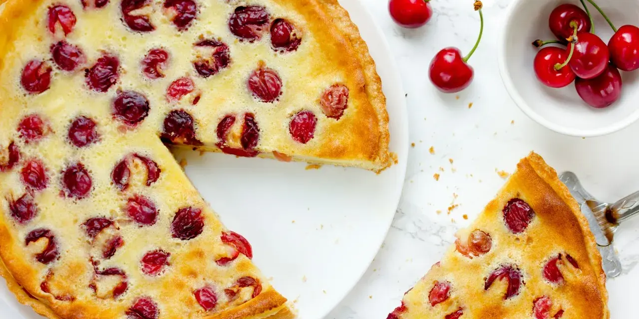 Ein köstlicher Pudding Kirsch Kuchen, mit frischen Kirschen belegt und goldbraun gebacken. Ein Stück wird gerade serviert.