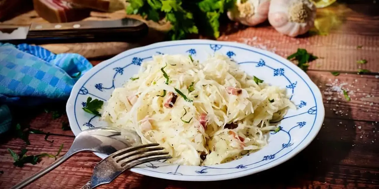 Ein Teller mit Krautsalat, garniert mit Petersilie. Daneben liegen Gabel und Löffel. Ein leckeres Krautsalat Rezept für dich!