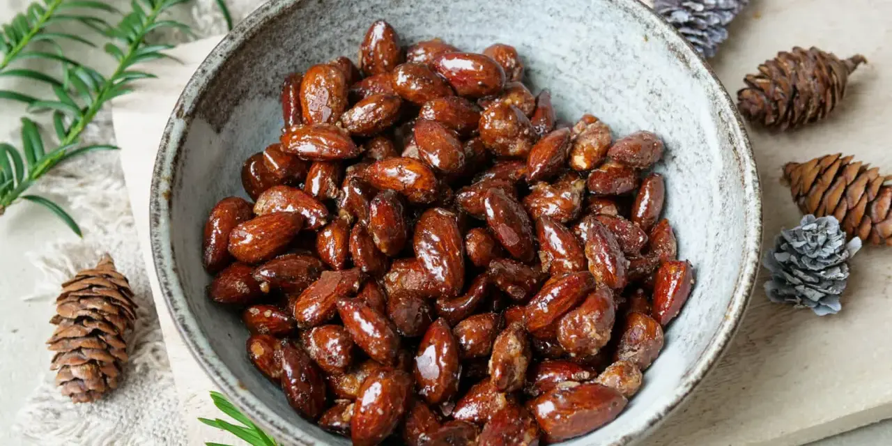 Schüssel mit glasierten, gebrannten Mandeln, zubereitet im Airfryer. Dekoriert mit Tannenzapfen und Tannenzweigen.