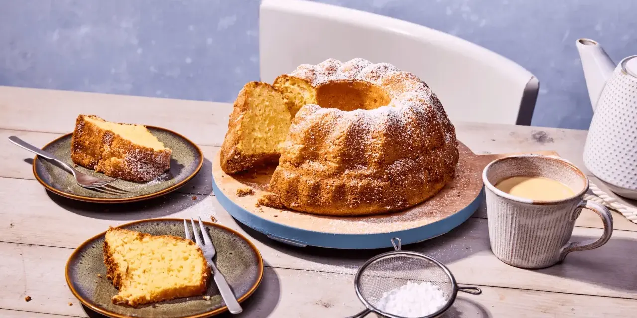 Ein goldbrauner Kartoffelkuchen mit Puderzucker bestreut, daneben zwei Teller mit Kuchenstücken, eine Tasse Kaffee und eine Kanne. Ein tolles Kartoffelkuchen Rezept!