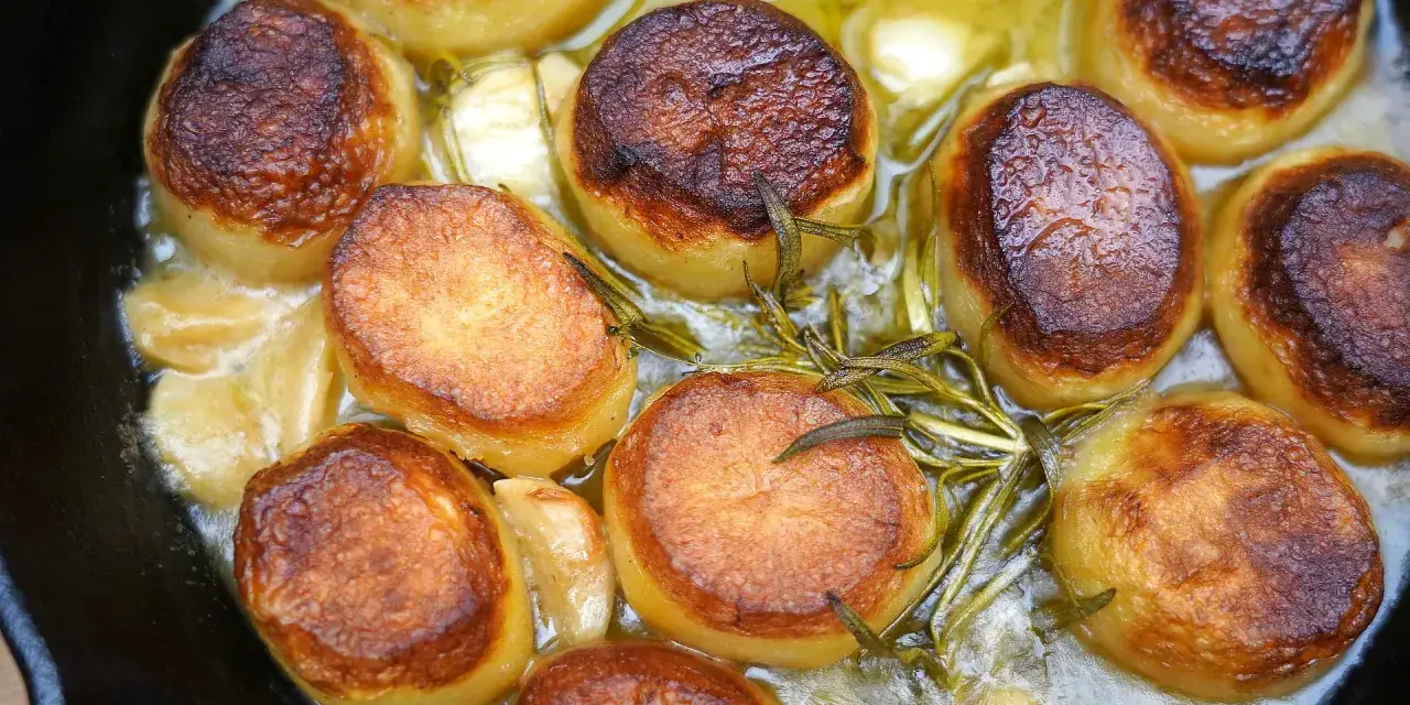 Saftige Fondant Kartoffeln mit Rosmarin und Knoblauch in einer Gusseisenpfanne, goldbraun gebraten.