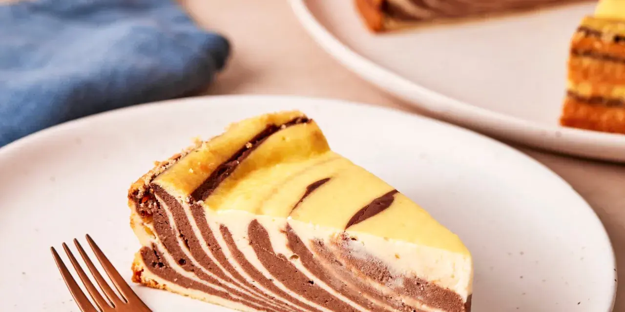 Ein Stück Zebrakuchen mit Quark, das auf einem Teller liegt, daneben eine Gabel.