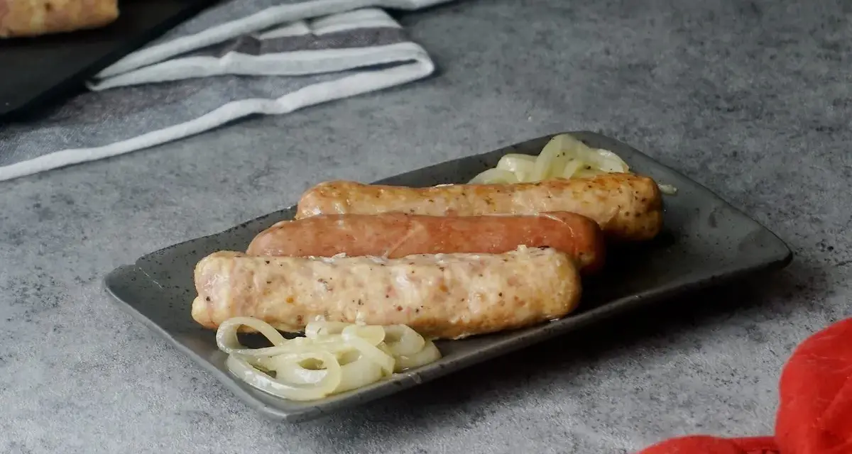 Drei Bratwürste mit Zwiebeln auf einem Teller, bereit zum Servieren. Sie sehen aus, als wären sie gerade aus dem Backofen gekommen.