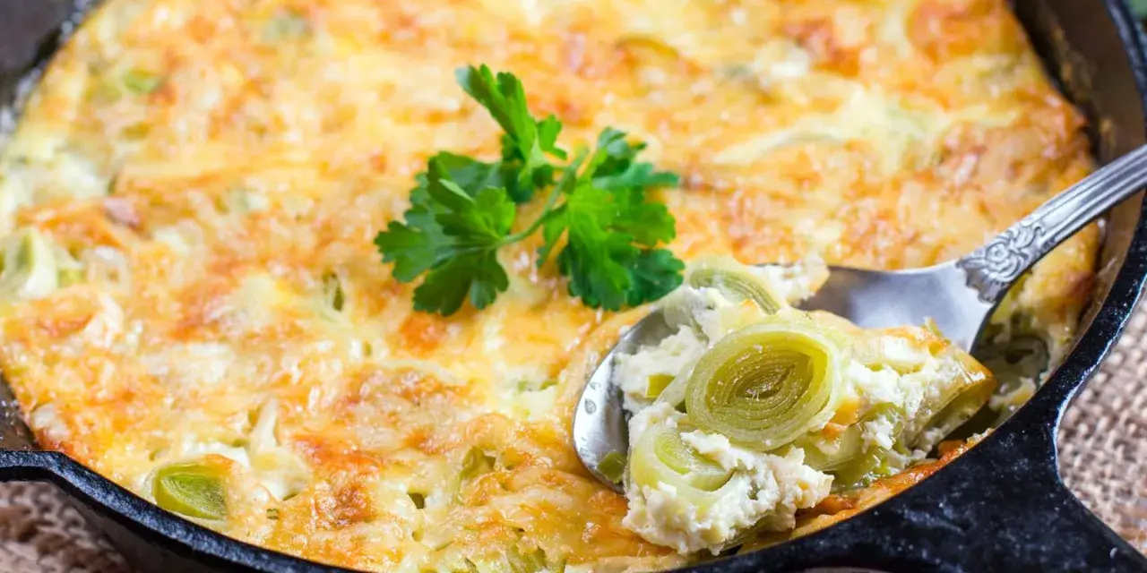 Ein goldbraunes Kartoffel-Lauch-Gratin in einer Gusseisenpfanne, mit einem Löffel herausgenommen, garniert mit Petersilie.