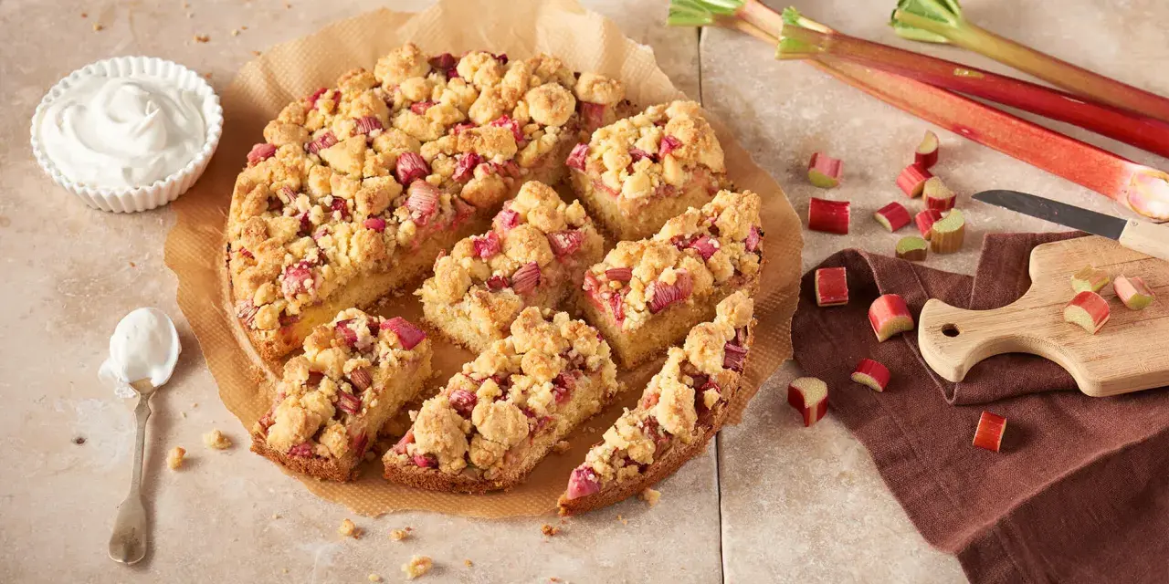 Ein saftiger Rhabarberkuchen mit Streuseln, perfekt für ein Rhabarberkuchen Rezept. Dazu eine Schüssel Schlagsahne.