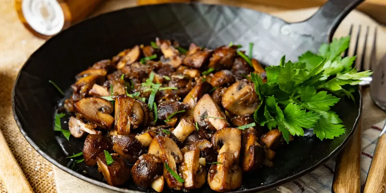 Gebratene Champignons in einer Pfanne, garniert mit frischer Petersilie. Ein köstliches Gericht, das zum Genießen einlädt.