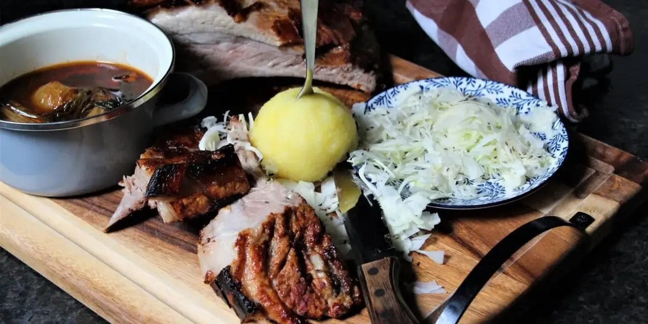 Deftige dicke Rippe mit Klößen, Sauerkraut und dunkler Soße auf Holzbrett.