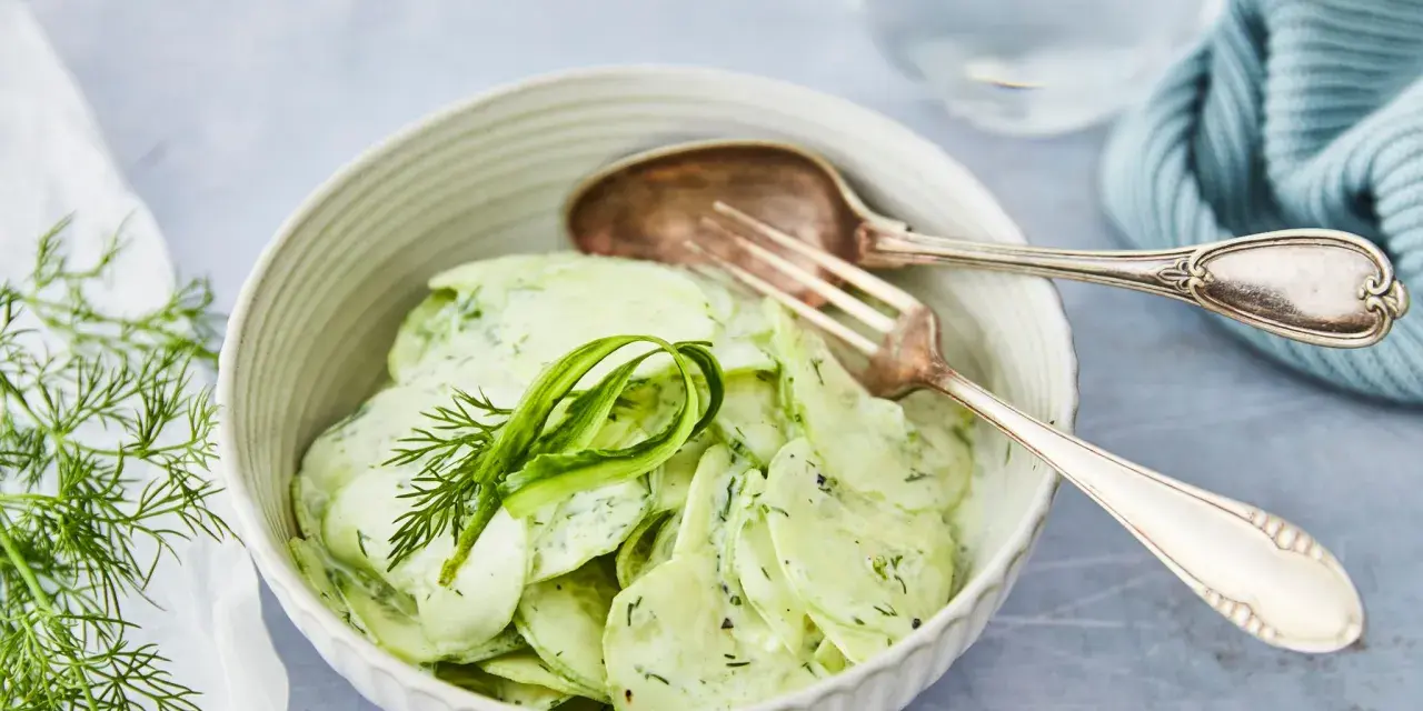 Omas Gurkensalat mit Joghurt, cremig und frisch, garniert mit Dill. Ein Löffel und eine Gabel liegen bereit.