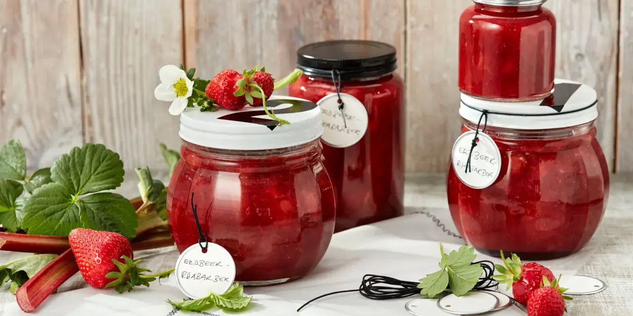 Gläser mit Erdbeer-Rhabarber-Marmelade, garniert mit frischen Erdbeeren und Blüten.