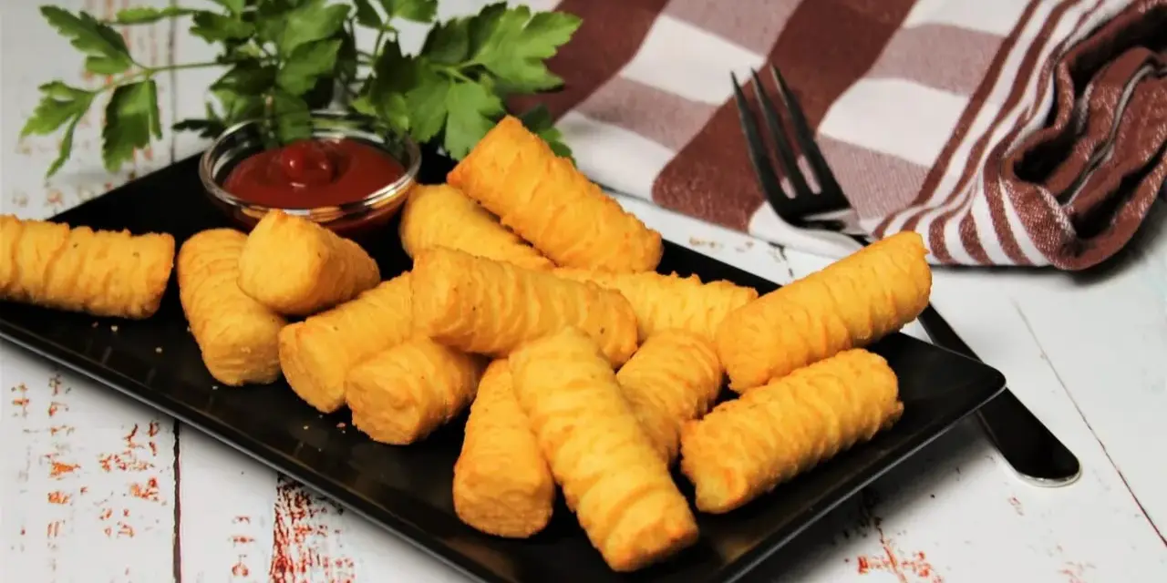 Goldbraune Kroketten, frisch zubereitet, liegen auf einem schwarzen Teller. Dazu gibt es Ketchup und frische Petersilie. Perfekt, um Kroketten selber machen zu lernen!
