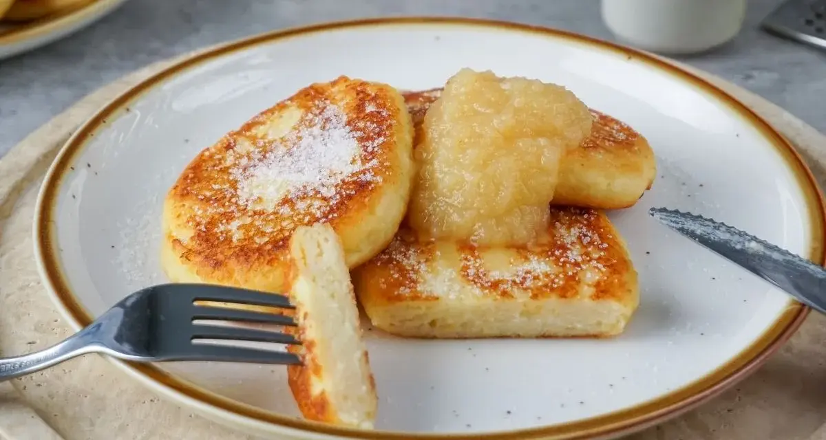 Goldbraune Quarkkeulchen, bestreut mit Puderzucker, serviert mit Apfelmus. Ein köstliches Quarkkeulchen Rezept zum Genießen.