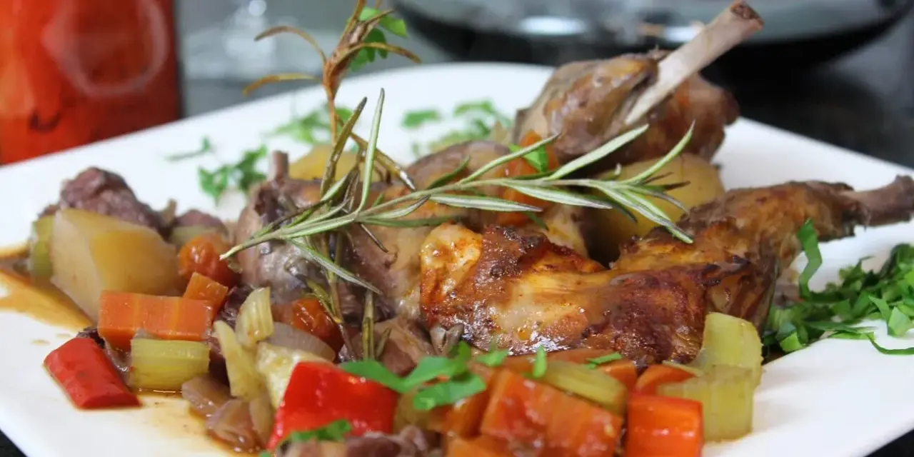 Klassisches Kaninchen-Rezept: Zartes Kaninchen mit Wurzelgemüse und Rosmarin auf einem weißen Teller serviert.