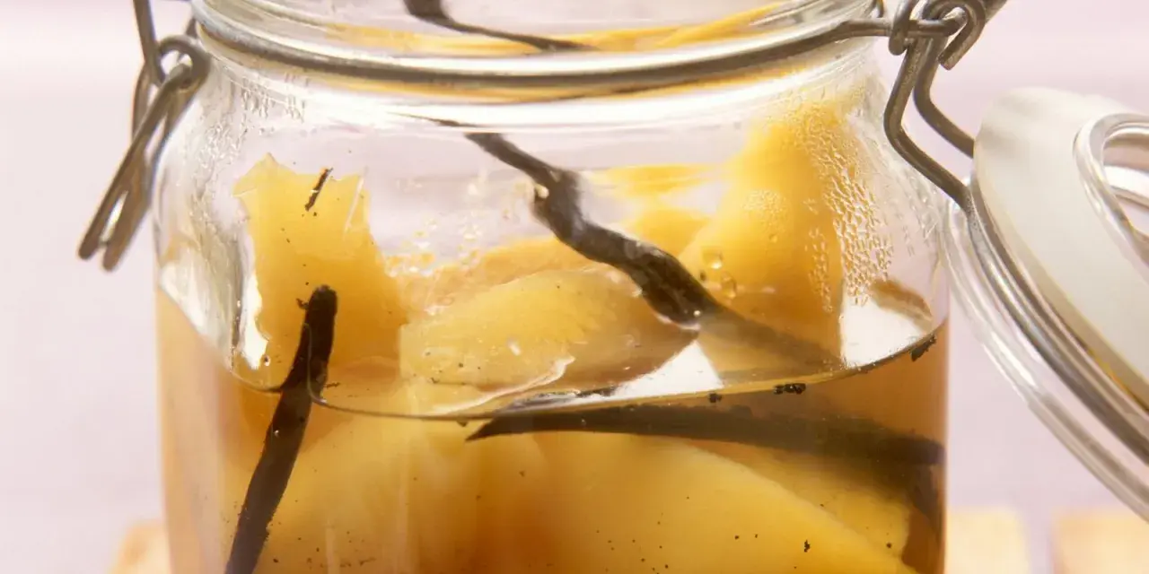 Ein Glas mit Quittenkompott, verfeinert mit Vanilleschoten. Die Fruchtstücke schimmern golden im Sirup.