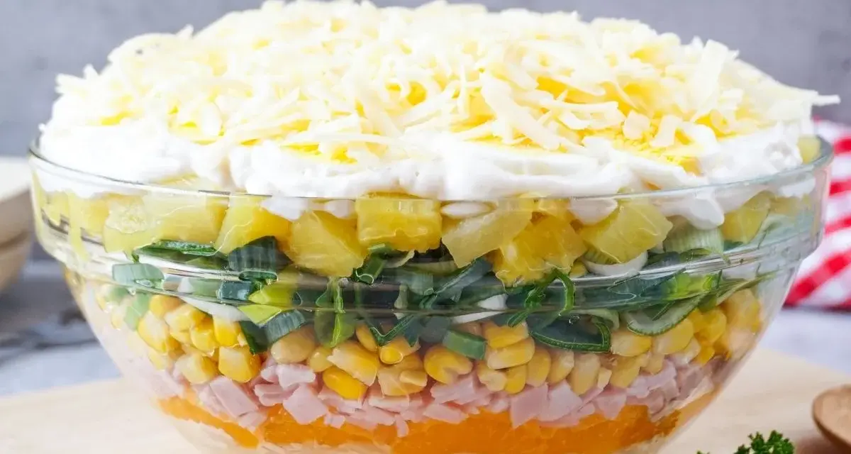 Schichtsalat rezept: Ein bunter Schichtsalat in einer Glasschüssel mit Ananas, Lauch, Mais, Schinken, Orange, Ei und Käse.